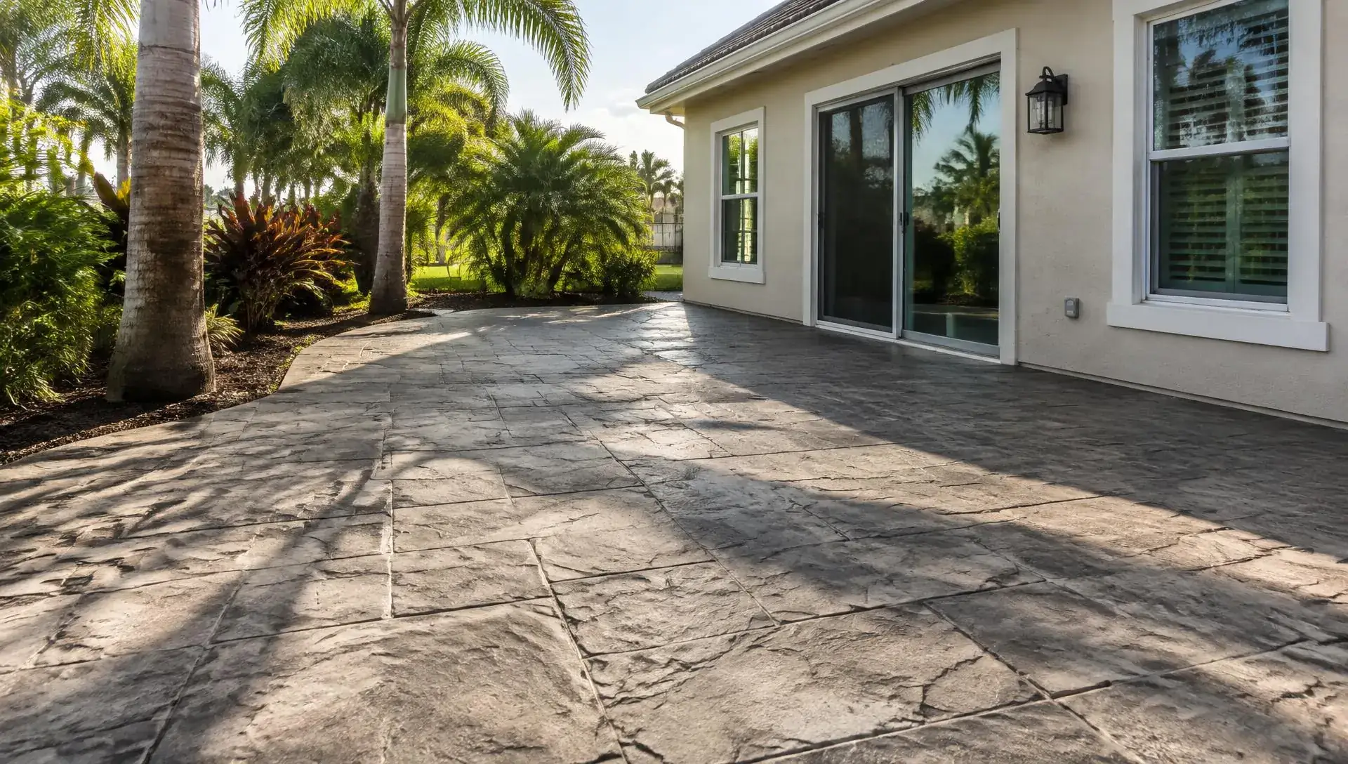 Gray stamped concrete patio with a stone-like texture curving along palms beside a stucco home