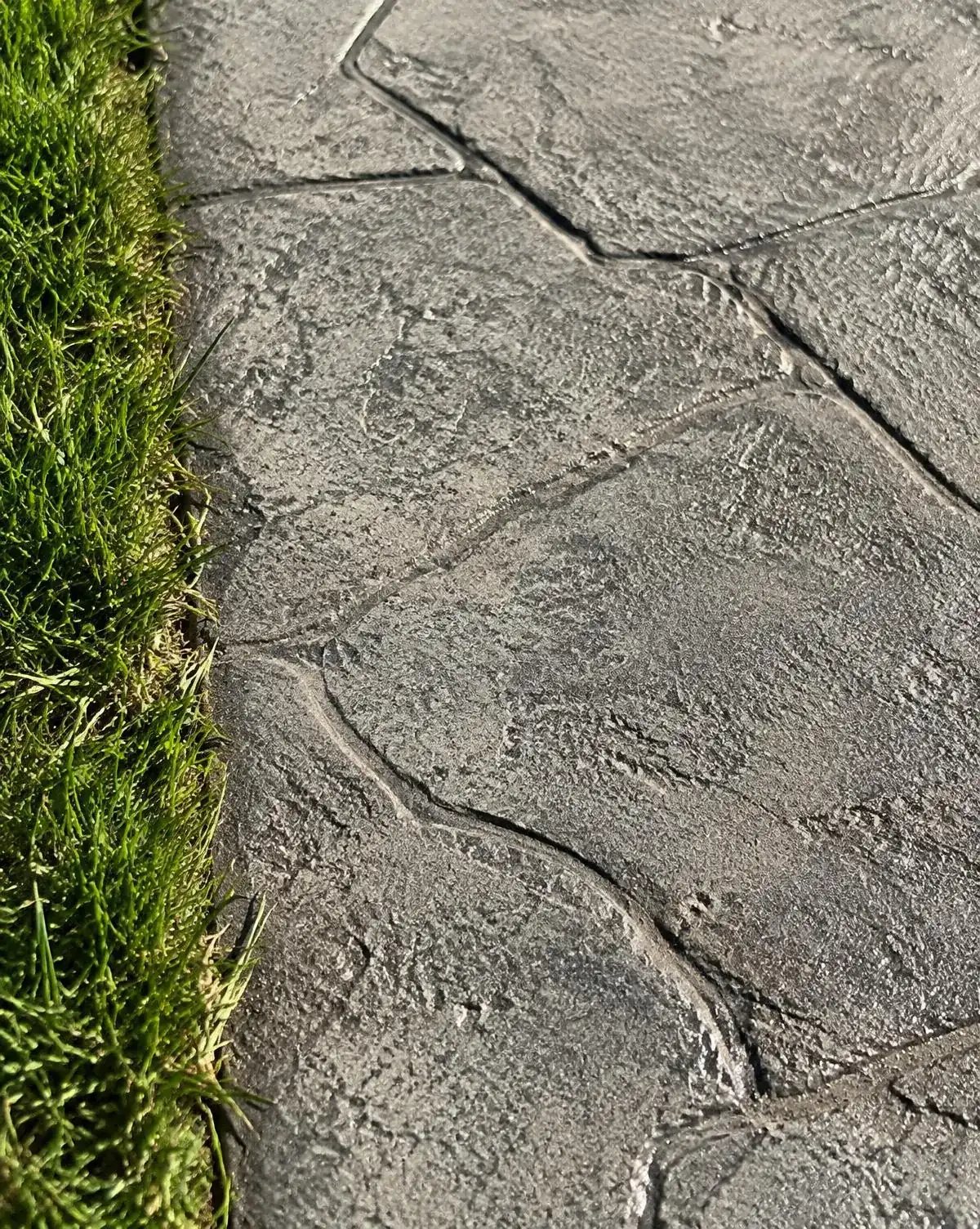 Close view of a textured decorative concrete surface with stone-like joints beside a strip of lawn